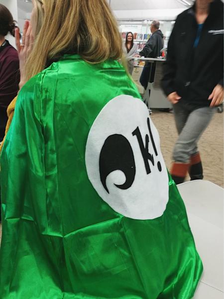 Super Librarian! Photo of a Toi Ohomai staff member wearing a bright green cape with a large koha logo on it