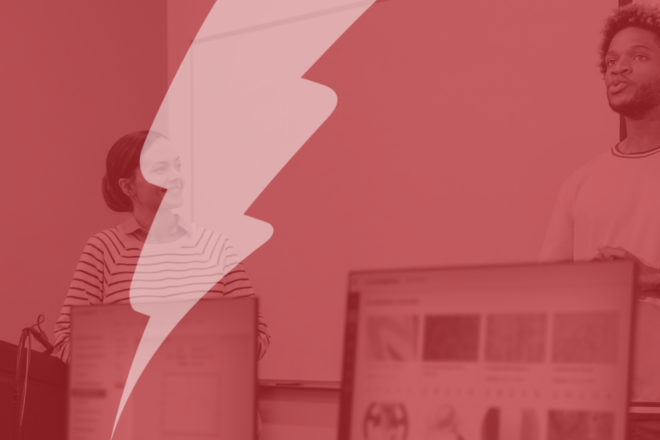 A red-tinted image of two students or educators presenting at the front of a computer lab classroom, with digital content displayed on monitors in the foreground. A large semi-transparent lightning bolt overlays the image, symbolising Catalyst’s focus on empowering digital learning.