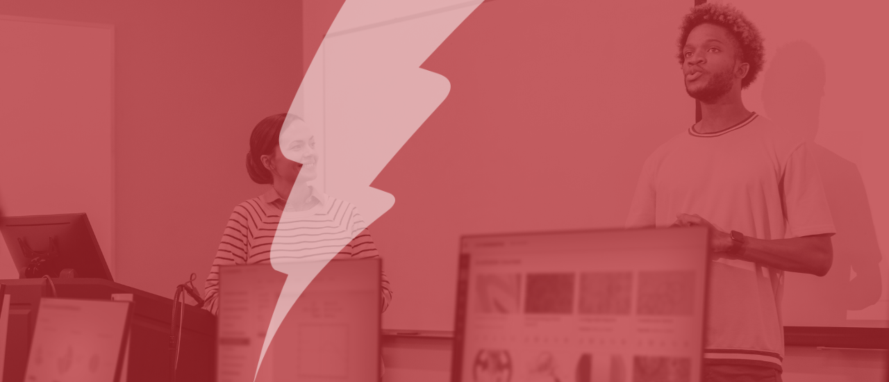 A red-tinted image of two students or educators presenting at the front of a computer lab classroom, with digital content displayed on monitors in the foreground. A large semi-transparent lightning bolt overlays the image, symbolising Catalyst’s focus on empowering digital learning.